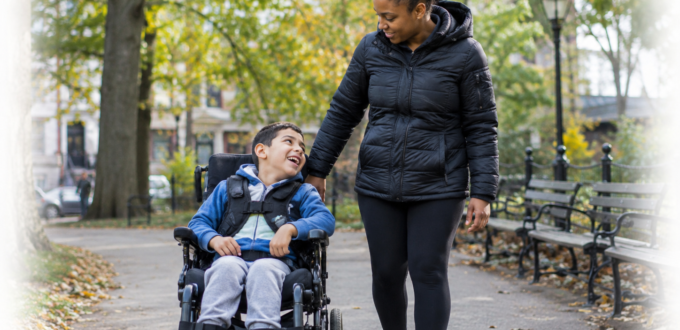 Autistic child using a wheelchair with a caregiver in a New York City park.